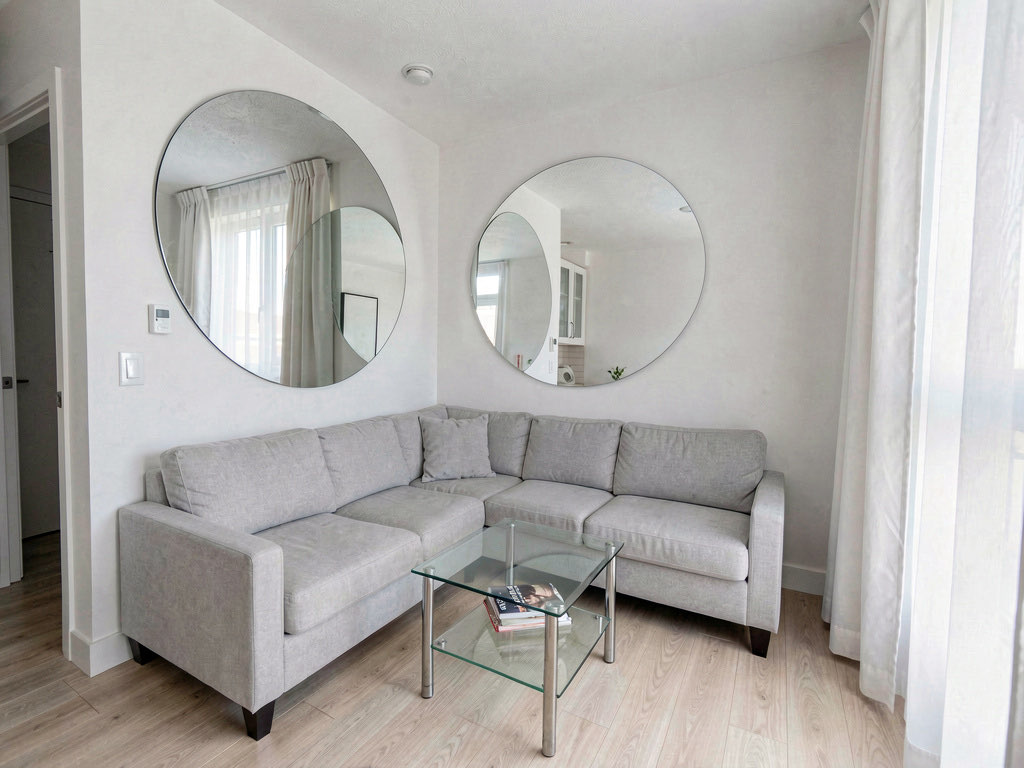 A small apartment living room using mirrors and light colors to feel larger, with a large round mirror reflecting the window