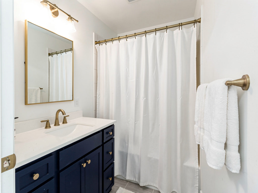 A budget bathroom remodel result with navy blue painted vanity, brushed gold hardware, new light fixture, and fresh white walls