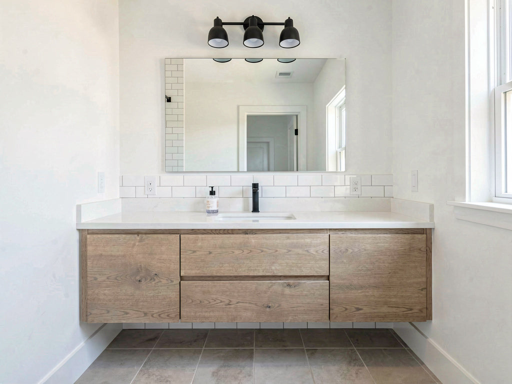 A bathroom with a new 48-inch floating oak vanity, white quartz countertop, large frameless mirror, and modern light fixture