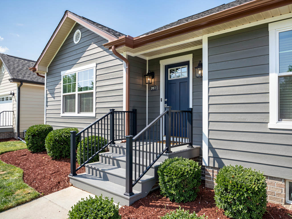 The same house exterior after renovation with new fiber cement siding, navy door, and clean landscaping