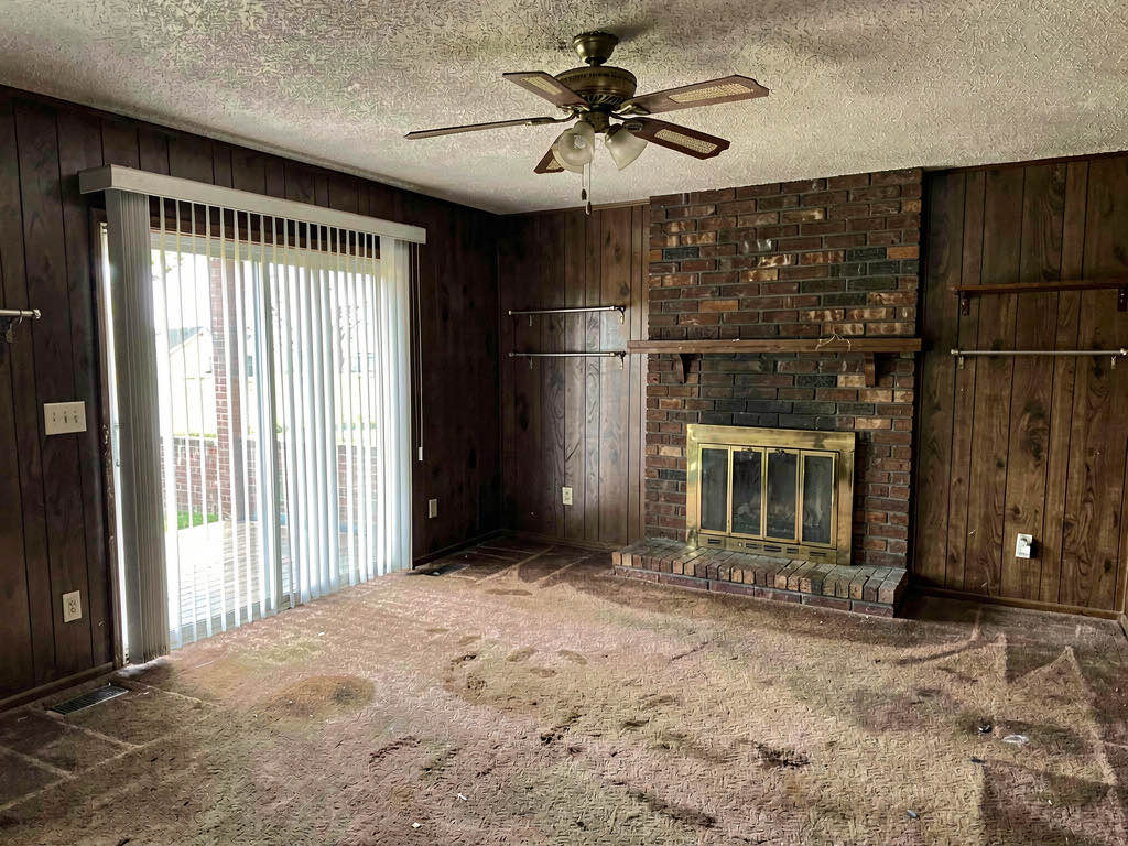 A dated living room with dark wood paneling, worn carpet, and popcorn ceiling ready for a flip
