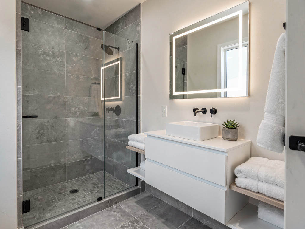 A renovated spa-like bathroom with gray porcelain tile, floating vanity, and glass shower enclosure
