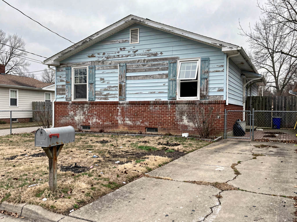 A neglected house exterior with faded siding, dead lawn, and mismatched shutters before a flip