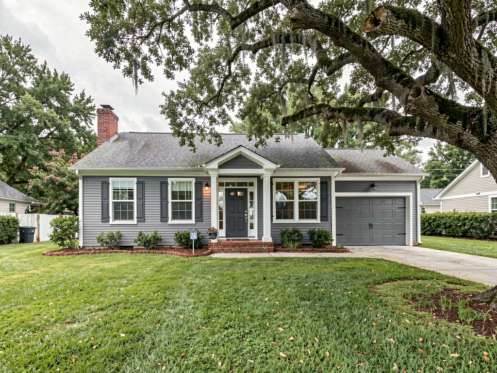 A colonial house painted medium gray with white trim and window frames, a dark gray front door, green lawn and mature oak tree