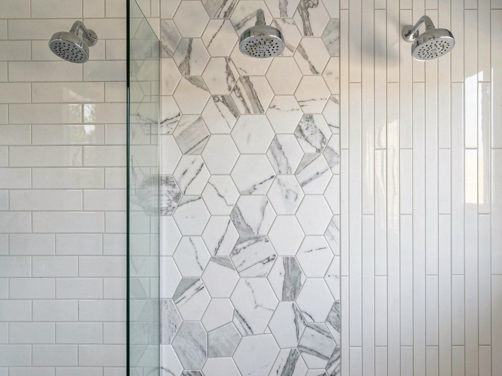 Three different bathroom tile patterns side by side — subway, hexagonal marble, and vertical stacked elongated tiles with the same chrome showerhead