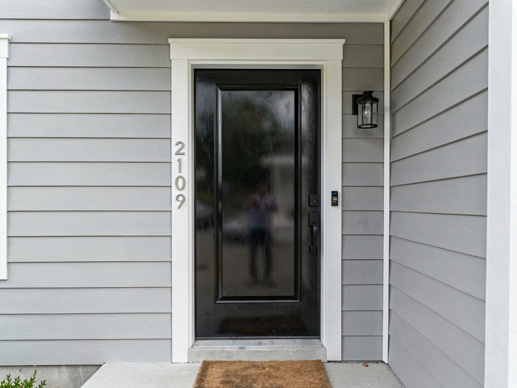 Glossy black front door on a light gray house with modern hardware and brushed nickel house numbers