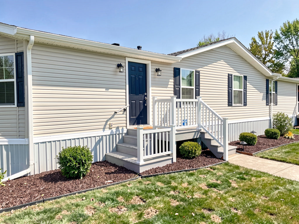 Mobile home exterior with new vinyl skirting, navy blue front door, composite deck, and clean landscaping