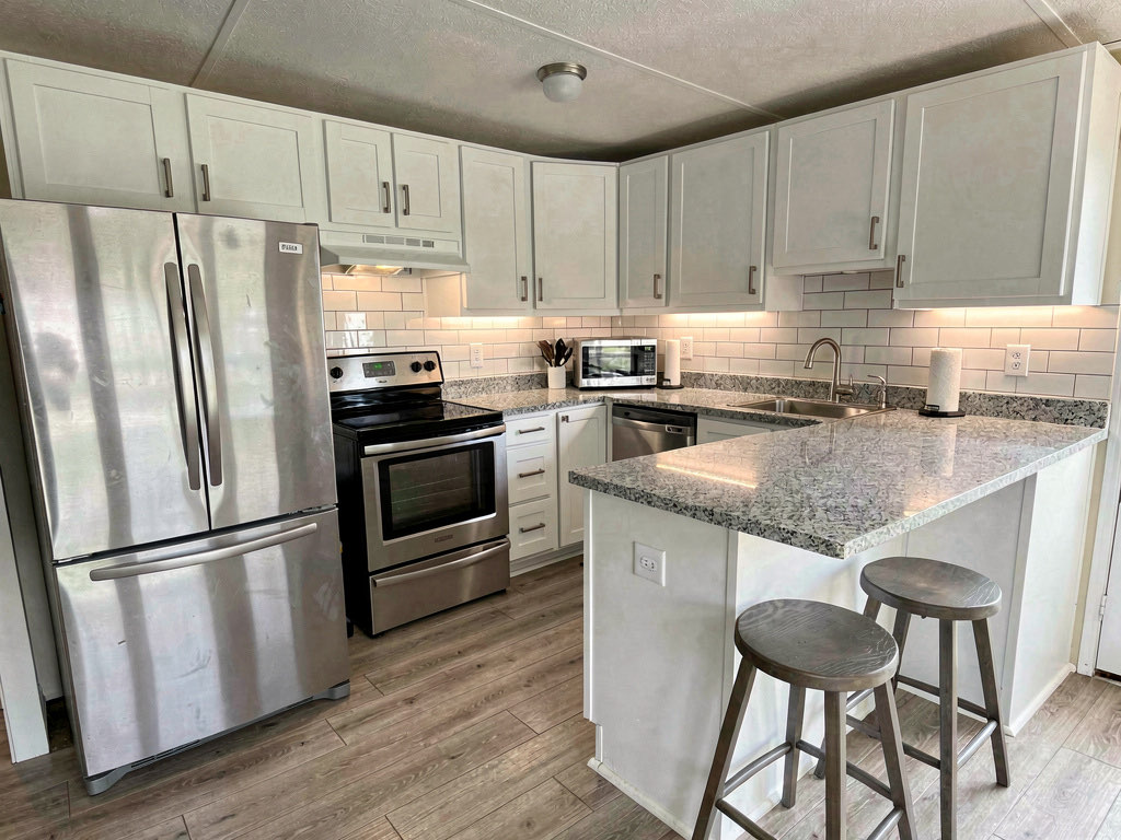 Remodeled mobile home kitchen with white painted cabinets, granite countertops, subway tile backsplash and brushed nickel hardware
